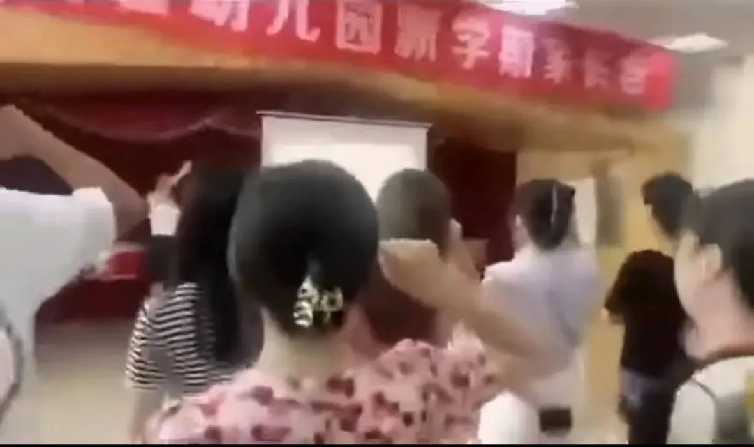 台上的幼儿园老师正领着一群学生家长集体宣誓：“我将无条件地配合老师” ...