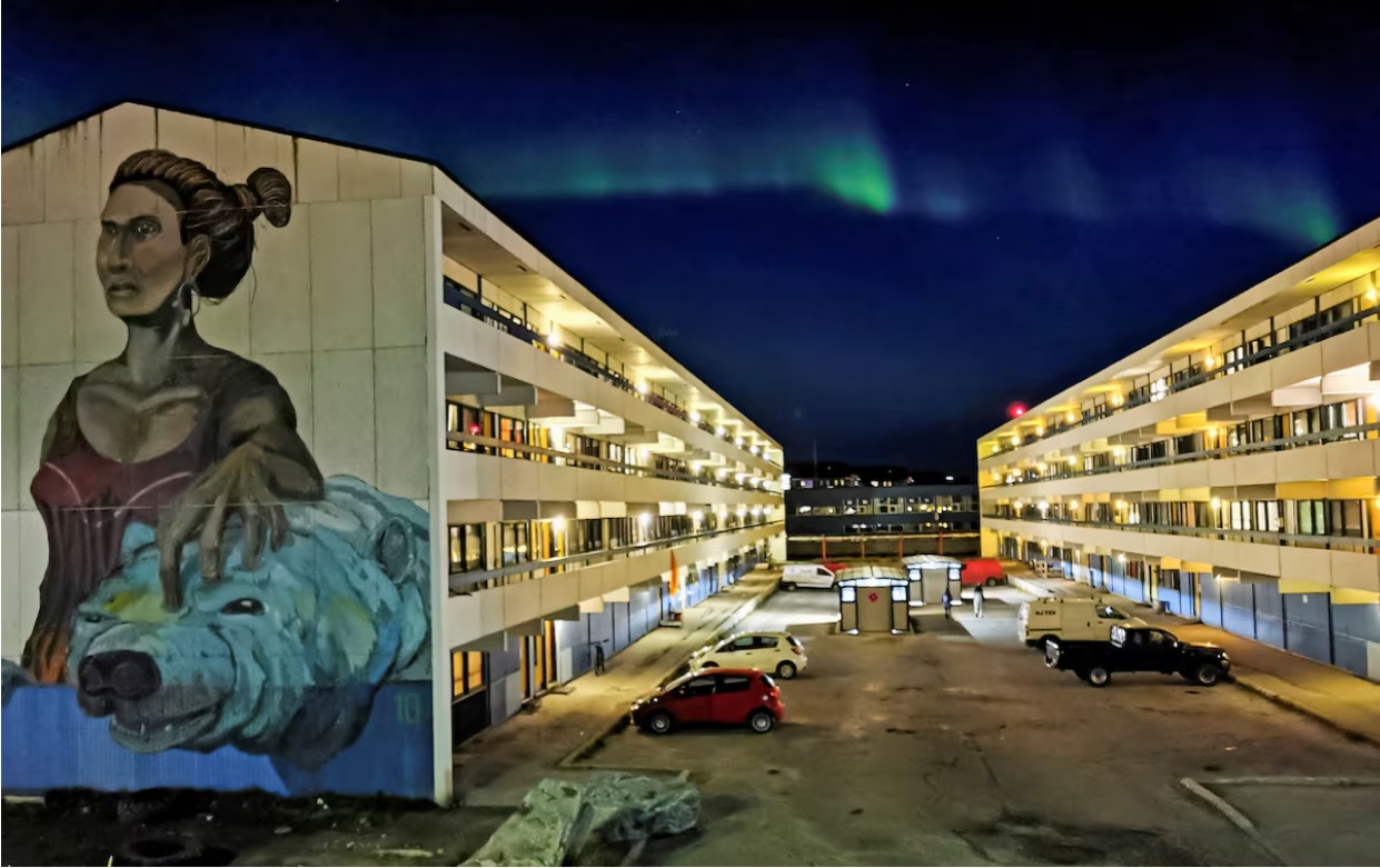 在格陵兰岛努克，一栋绘有壁画的社会住房建筑后方，可以看到北极光